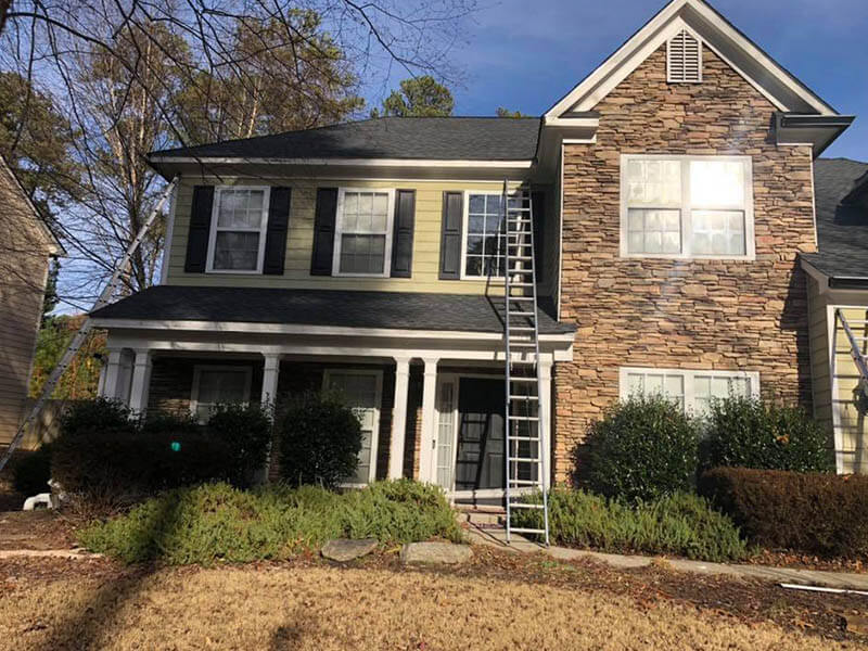 Professional Gutter Cleaning crew working on a two-story Atlanta home with ladders staged safely on the ground